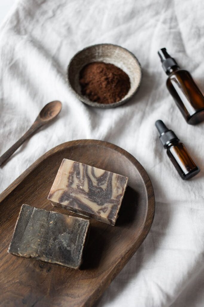 From above of stylish soaps placed near aroma oils in small jars on white fabric in daytime